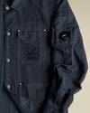 Dark blue jacket by Alessi with C.P. Company branding, snap buttons, and a sleeve lens detail.