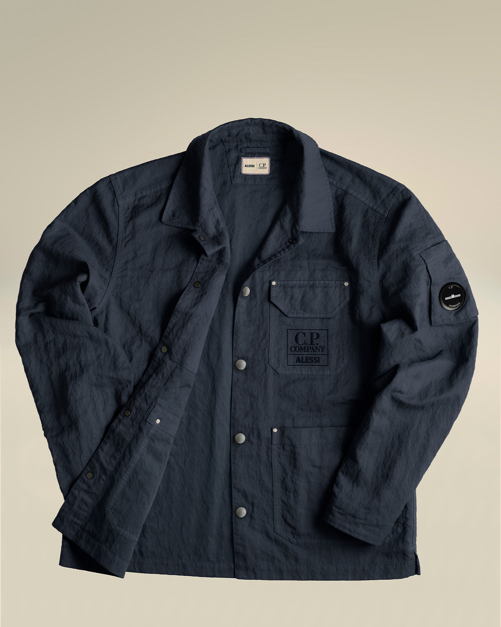 Dark blue crinkled jacket by Alessi featuring C.P. Company branding on chest and sleeve, laid flat.