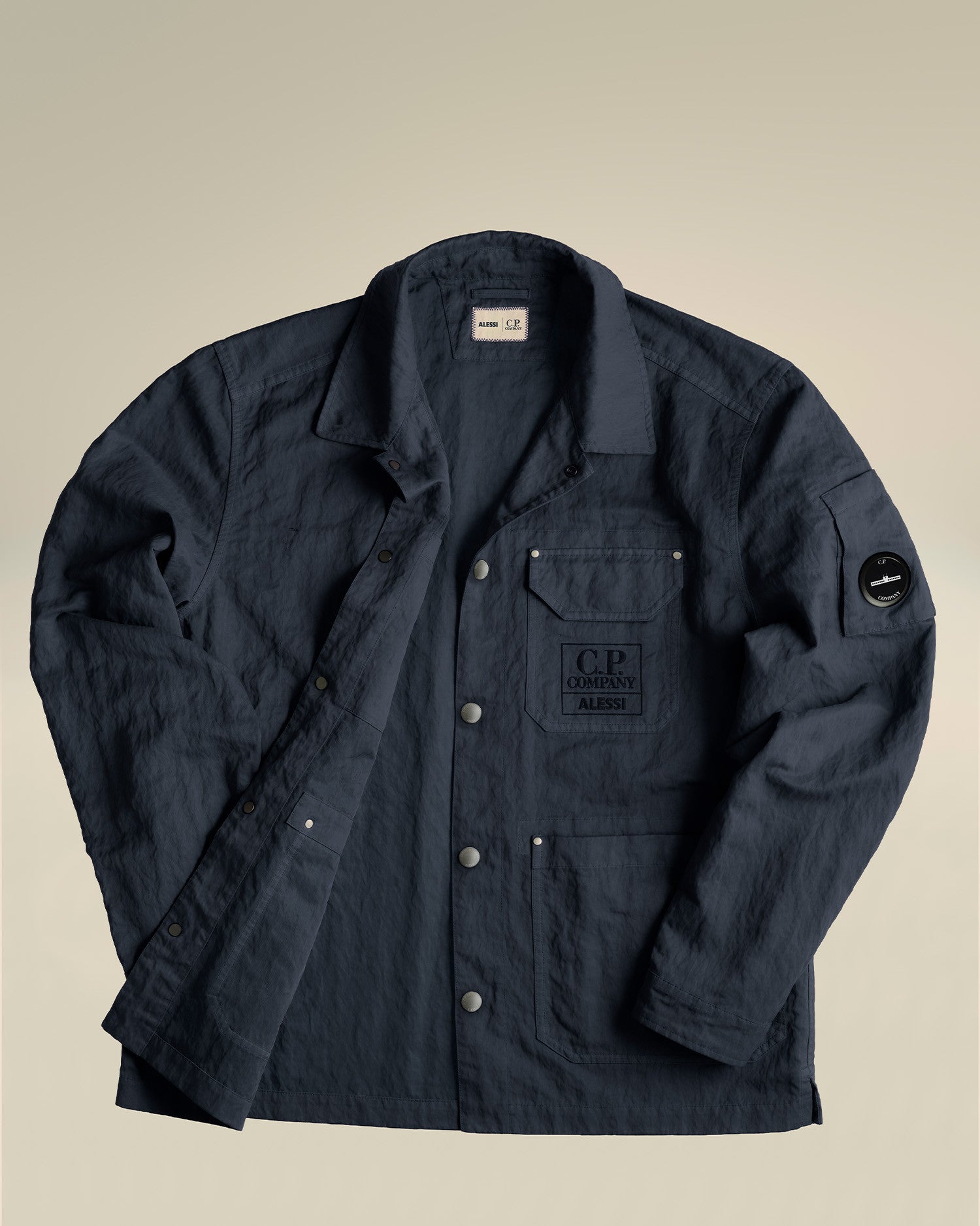 Dark blue crinkled jacket by Alessi featuring C.P. Company branding on chest and sleeve, laid flat.