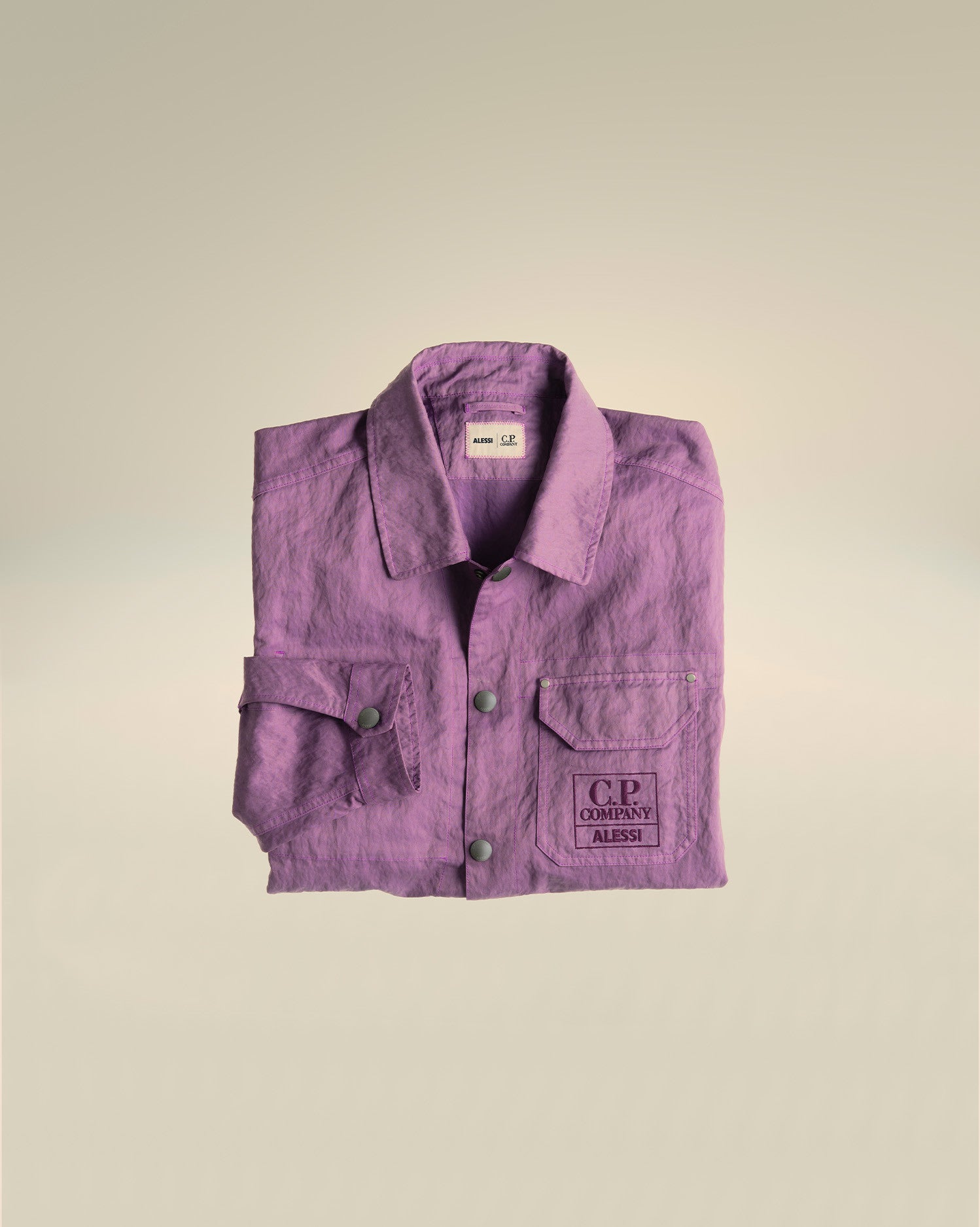 A purple crinkled utility jacket by Alessi, with two chest pockets and an embroidered C.P. Company Alessi logo.