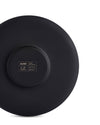 Dark matte black cup by Alessi, showing its underside with engraved brand, designer, and material details.