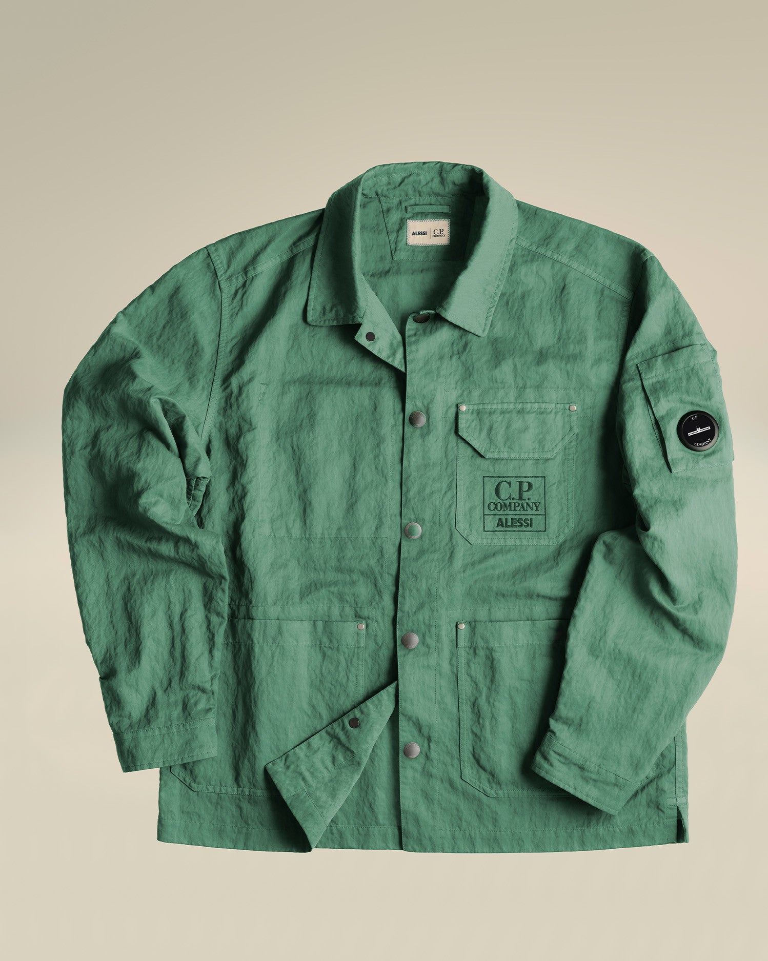 Dark green crinkled utility jacket by Alessi, with 'C.P. Company ALESSI' chest print, sleeve lens, and snap buttons.
