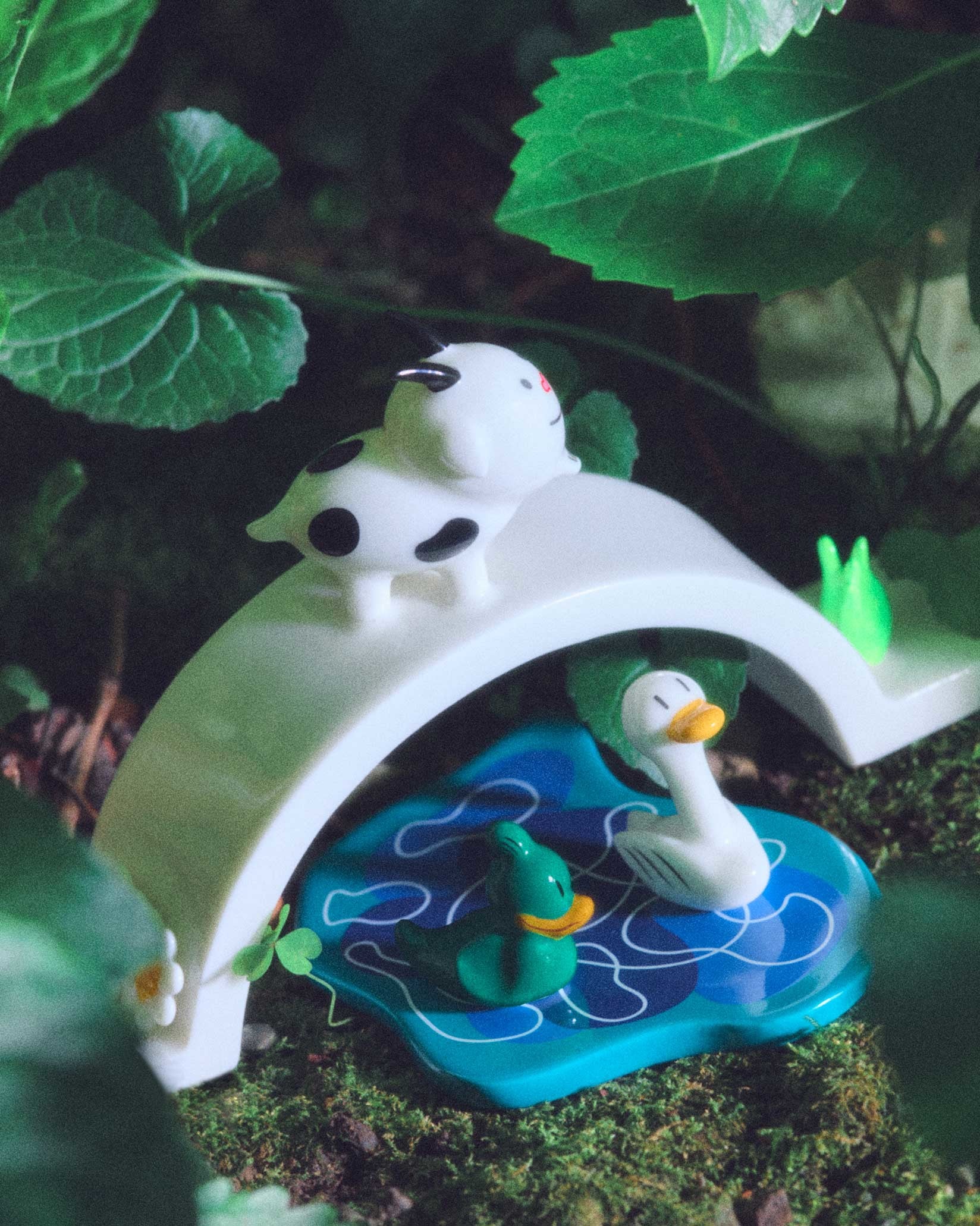 Ornamental figurines by Alessi, depicting a spotted cow on a white bridge over a blue pond with two ducks.