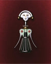 A silver, black, and mint green corkscrew by Alessi, designed as a stylized woman with a smiling face, on a deep red background.