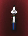 Silver and blue figure corkscrew by Alessi, with a conical hat, perforated torso, and striped base, centered on a dark red background.