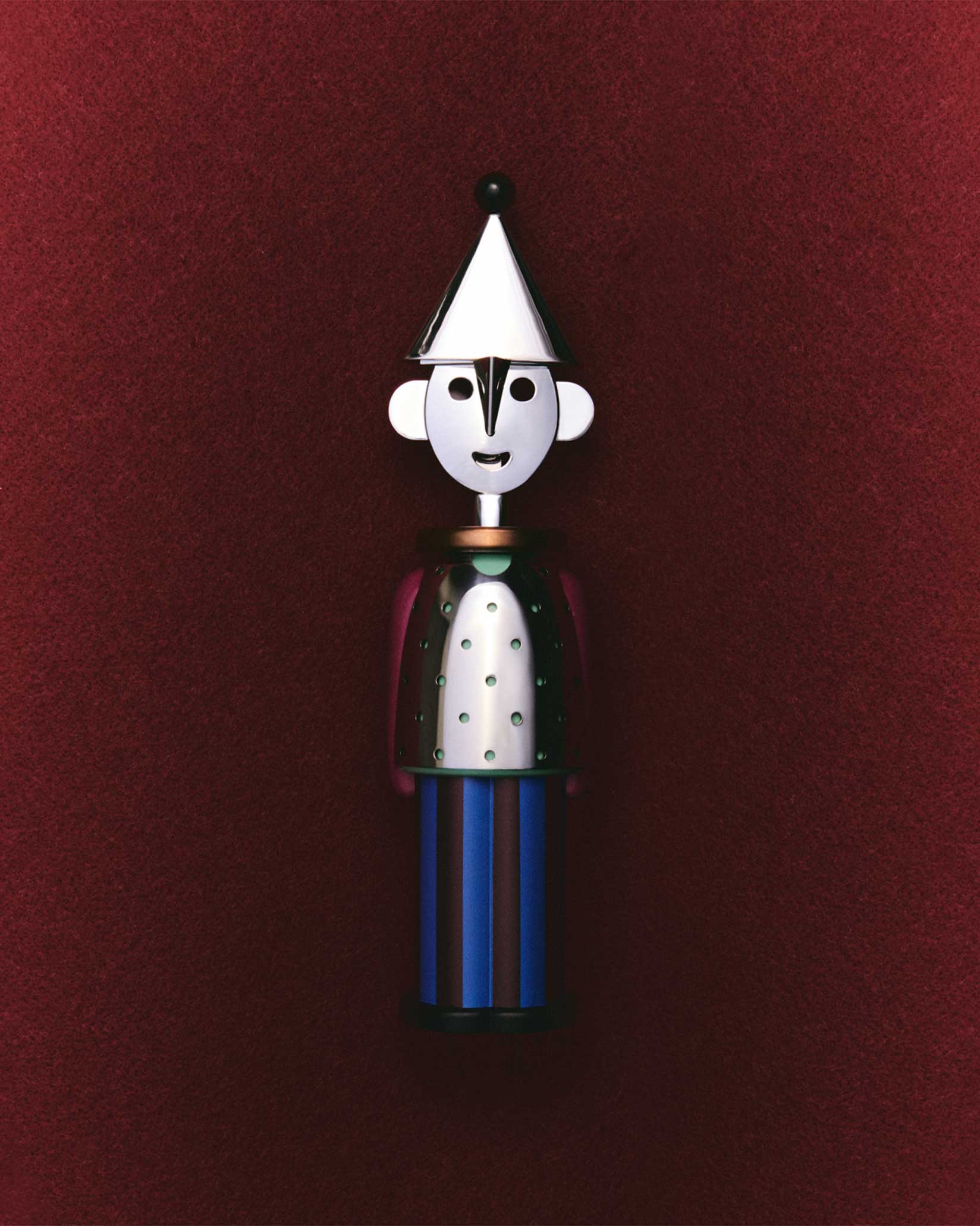 Silver and blue figure corkscrew by Alessi, with a conical hat, perforated torso, and striped base, centered on a dark red background.