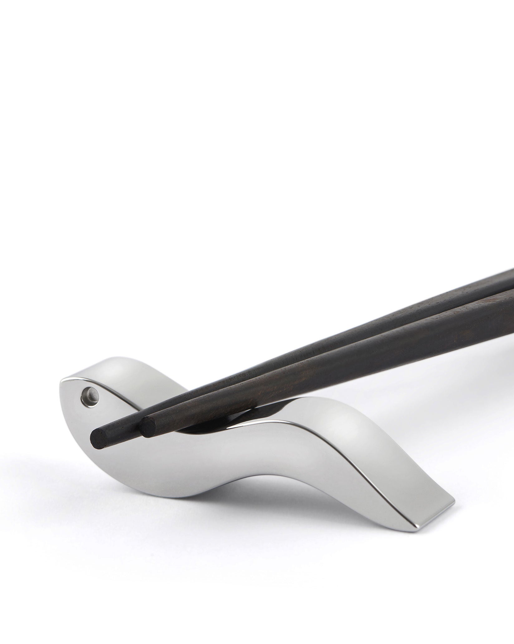 Dark wooden chopsticks by Alessi, resting on a sleek silver metallic holder.