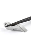 Silver metallic chopstick rest by Alessi holding two dark wooden chopsticks on a white background.