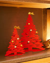 Red metal Christmas tree ornament set by Alessi featuring cutout branches, colorful baubles, and star toppers.
