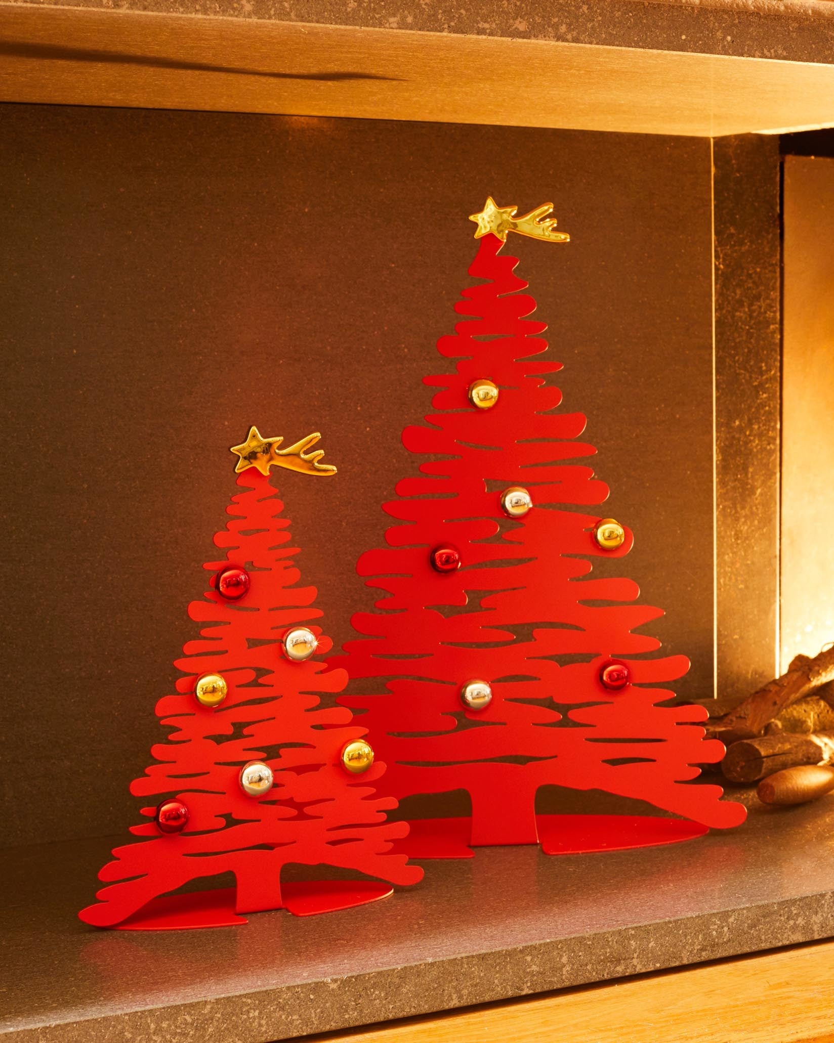 Red metal Christmas tree ornament set by Alessi featuring cutout branches, colorful baubles, and star toppers.