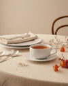 La Bella Tavola white cup by Alessi with a saucer and tea, on a neutral tablecloth with autumn decor.