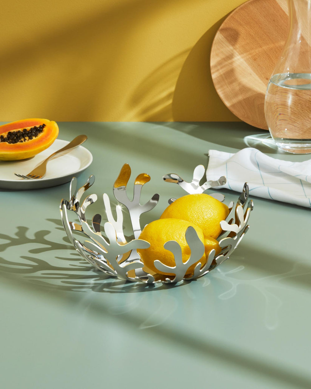 Silver-tone coral fruit holder by Alessi with organic cut-out design holding lemons on a table.