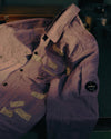 Purple crinkled jacket by Alessi with snap buttons, chest pockets, visible text patches, and a sleeve badge.
