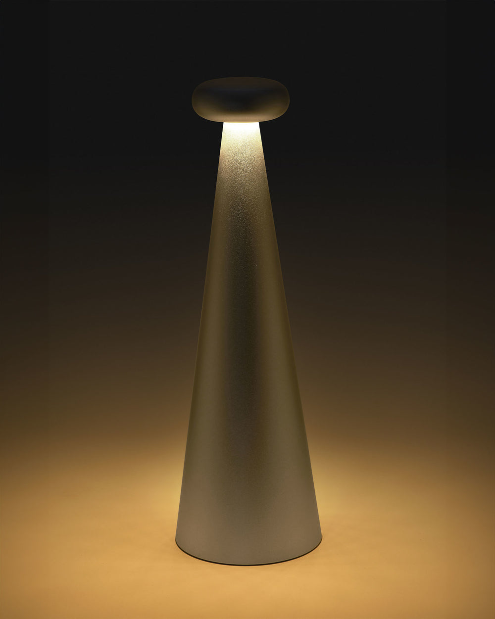 Conical matte gray table lamp by Alessi with a luminous mushroom-shaped top diffuser casting warm light.