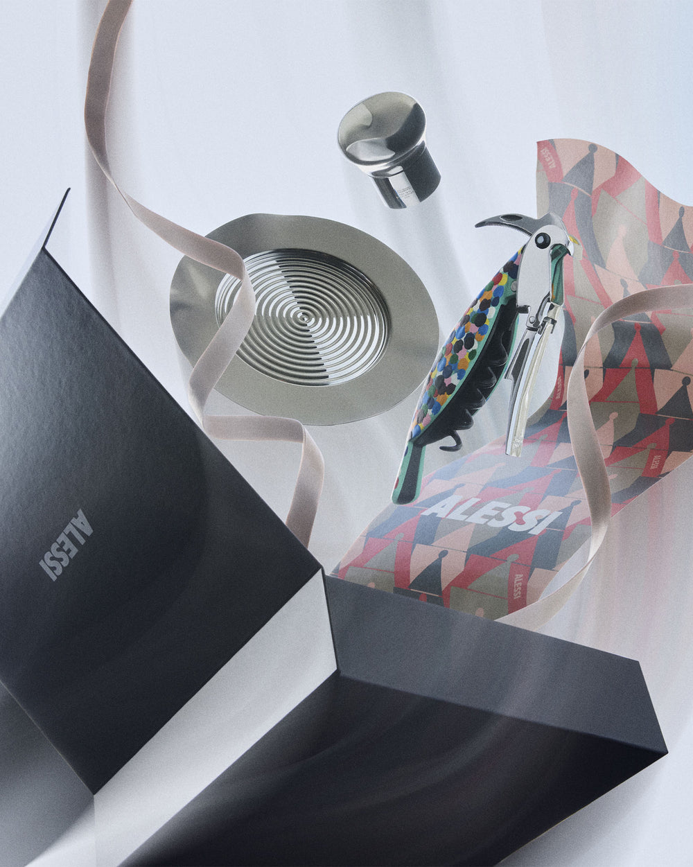 Colorful dotted parrot corkscrew, silver stopper, and coaster mixology set by Alessi, presented with a black box and geometric wrapping paper.