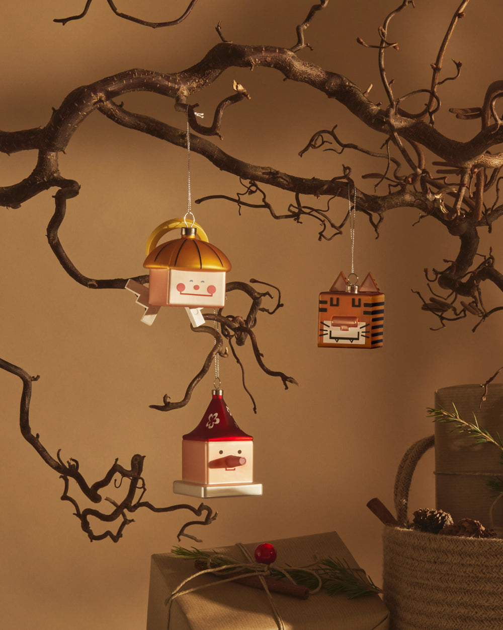 Orange square tiger Christmas tree ornament by Alessi, with black stripes and square ears, hanging from a bare branch.