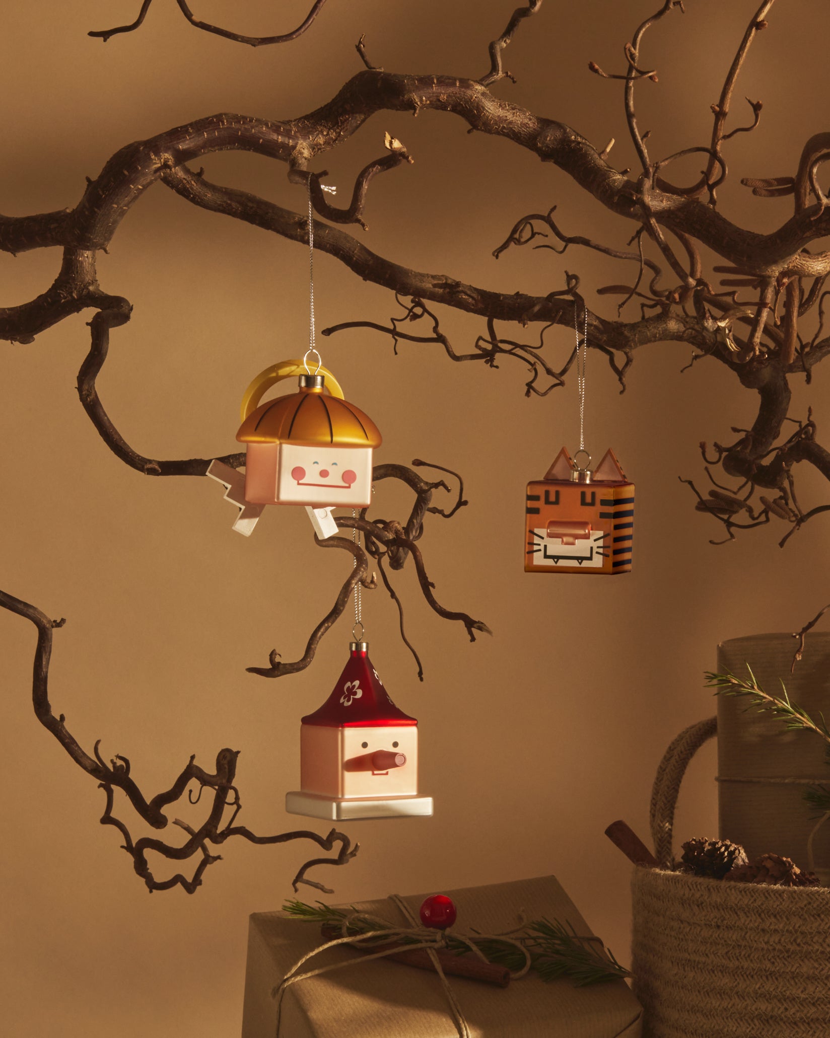 Orange square tiger Christmas tree ornament by Alessi, with black stripes and square ears, hanging from a bare branch.