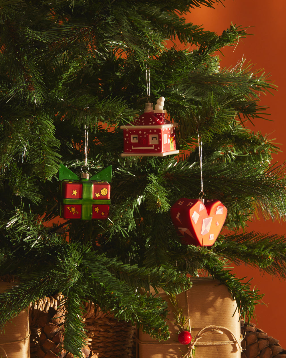 Red and green Cubetta gift box Christmas ornament by Alessi, adorned with gold stars and planets, hanging on a green tree.