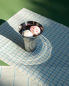 Silver metallic glass by Alessi with a fluted design, holding two scoops of ice cream on a grid-patterned tablecloth.