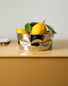 Silver-toned, irregularly shaped fruit bowl by Alessi, holding yellow lemons with green leaves.