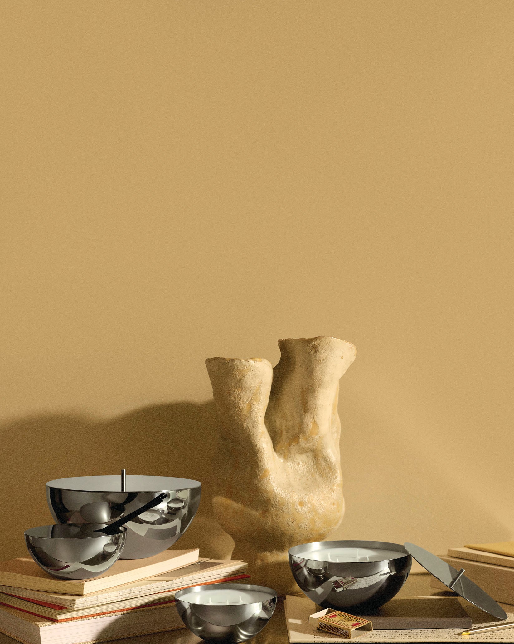 Polished metallic Rocc fragrance diffusers by Alessi arranged with a textured sculptural vase and books.