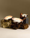Silver Rocc candle by Alessi, with multiple wicks, nestled among natural rocks and driftwood.