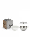 White Rocc candle by Alessi in a bowl, next to a stainless steel bowl and lid, with two branded packaging boxes.