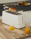 White ribbed toaster by Alessi heating a croissant on its warming rack, with orange juice.