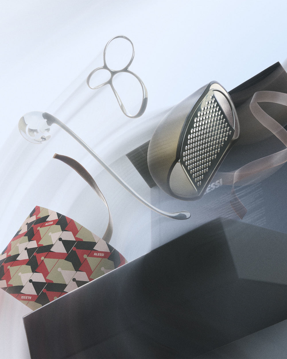 Dynamic gift set of pasta tools by Alessi, featuring a silver grater, clear pasta measure, and patterned packaging.