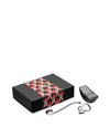 Black gift set by Alessi with a geometric patterned band, including a silver spoon, pasta measure, and grater.