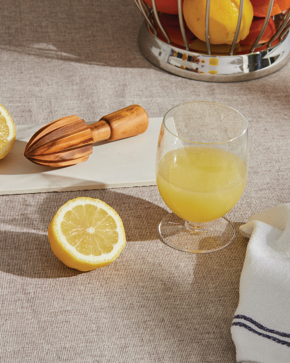 Wooden citrus-squeezer by Alessi on a white board with a lemon and glass of lemonade.