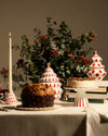 White ceramic Christmas tree-shaped centerpiece by Alessi, with red diamond patterns and a gold star on top, on a festive table.