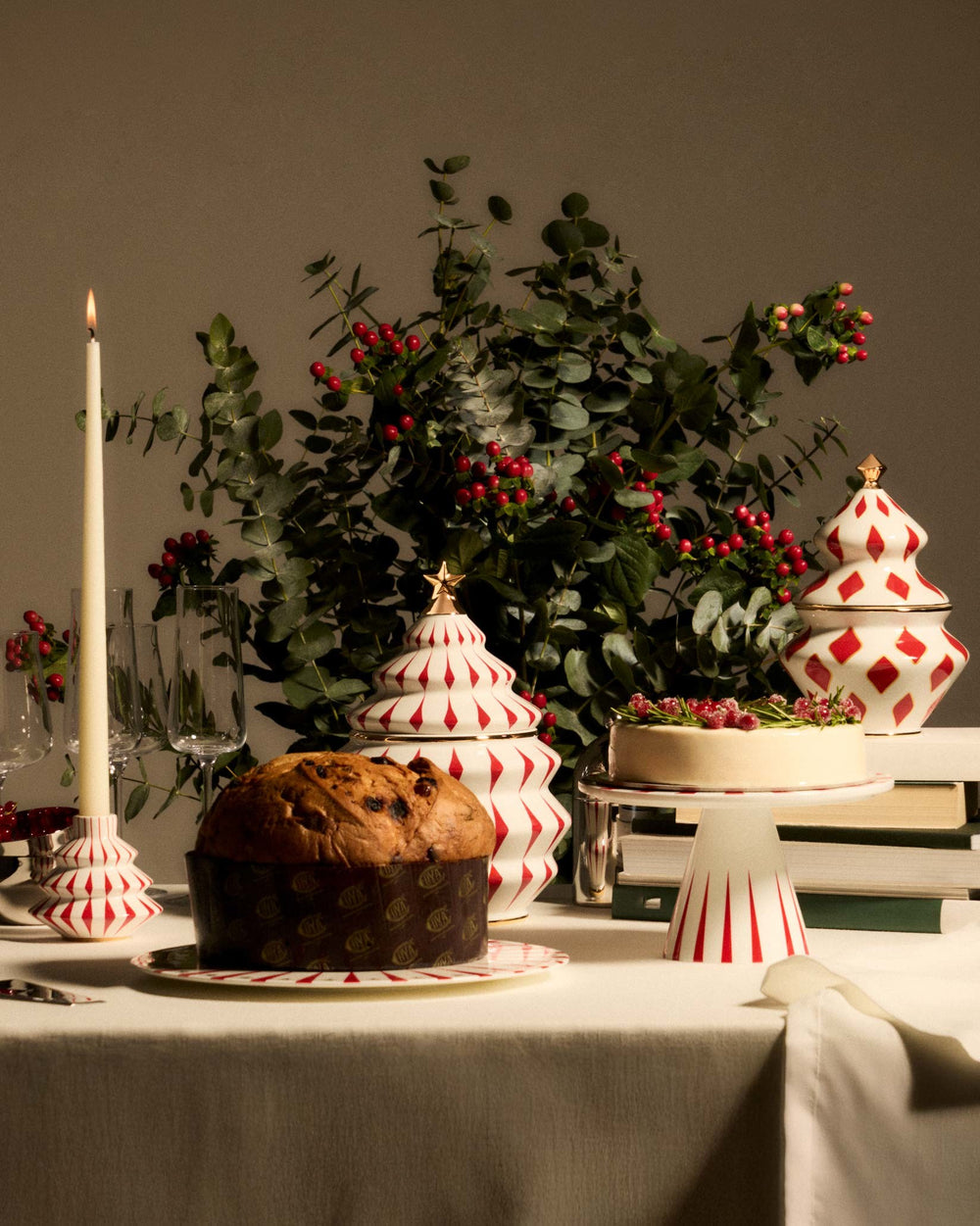 White and red tiered candlestick by Alessi, shaped like a Christmas tree with a diamond pattern, holding a lit candle.