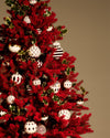 White, red, and gold Christmas tree ornaments by Alessi, with diverse patterns, hanging on a vibrant red fir tree.