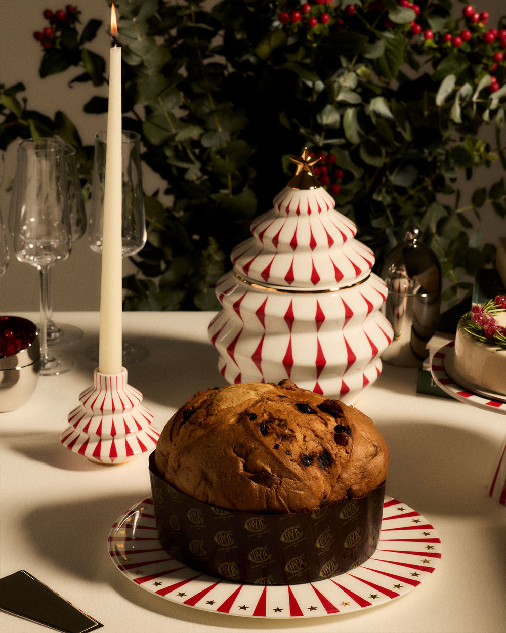 White tiered candlestick by Alessi with red vertical stripes, alongside a panettone and festive holiday decor.