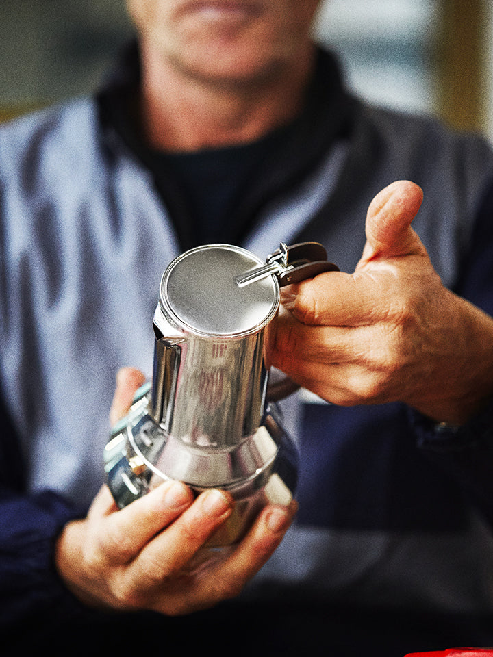 Man holding a shiny silver espresso maker with both hands, focusing on the top chamber and lever.