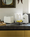 White fluted kitchen appliance set by Alessi, including a toaster, kettle, and lidded container on a dark countertop.