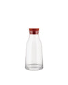 Clear glass pitcher with a reddish-brown stopper by Alessi, featuring a smooth, minimalist design.
