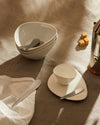 White ceramic Colombina collection by Alessi, featuring irregularly shaped bowls, plates, and modern cutlery on a linen tablecloth.