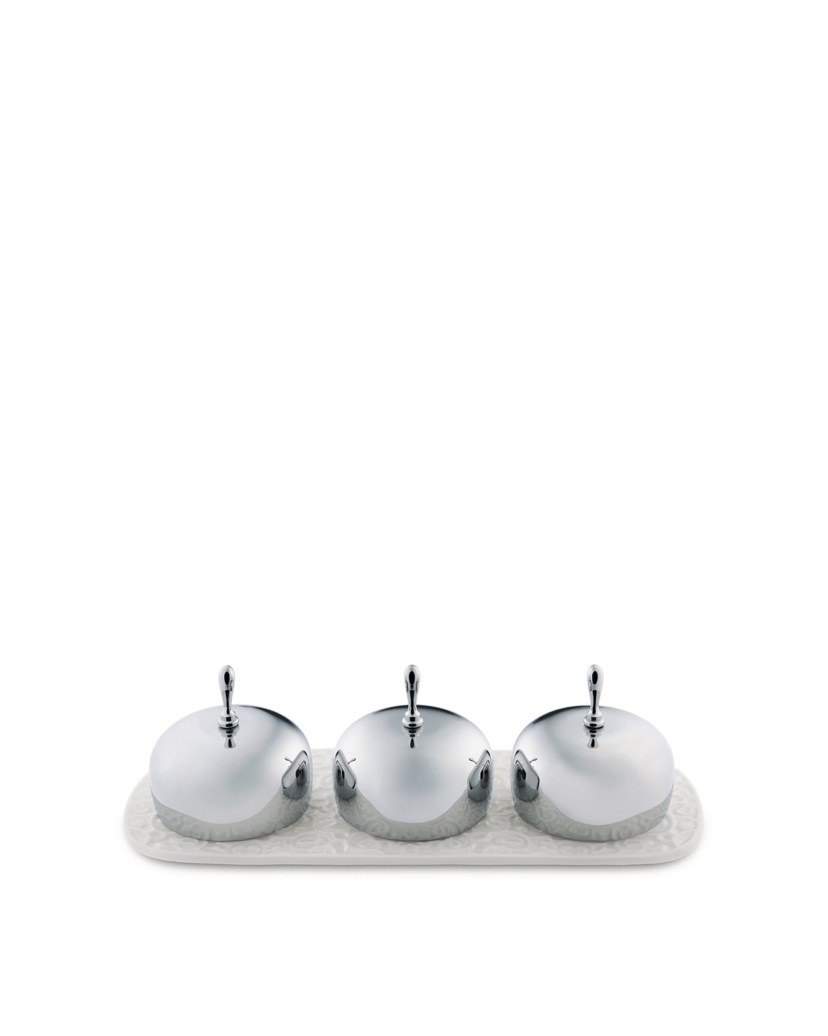 Shiny silver three-piece condiment set by Alessi with embossed container bases on a matching patterned white tray.