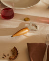 Wooden handle and silver metal bottle opener by Alessi, resting on a beige tablecloth next to a golden bottle cap.