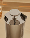 Silver metallic tending box by Alessi with a circular lid and three openings revealing internal coils, seen from above.