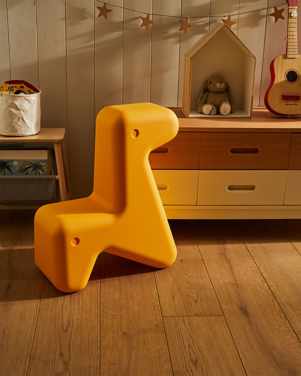 Bright yellow giraffe-shaped children's chair by Alessi, with rounded edges, in a sunlit room.