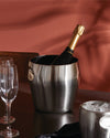 A brushed stainless steel champagne bucket by Alessi, holding a bottle, with an ice bucket and two empty wine glasses.