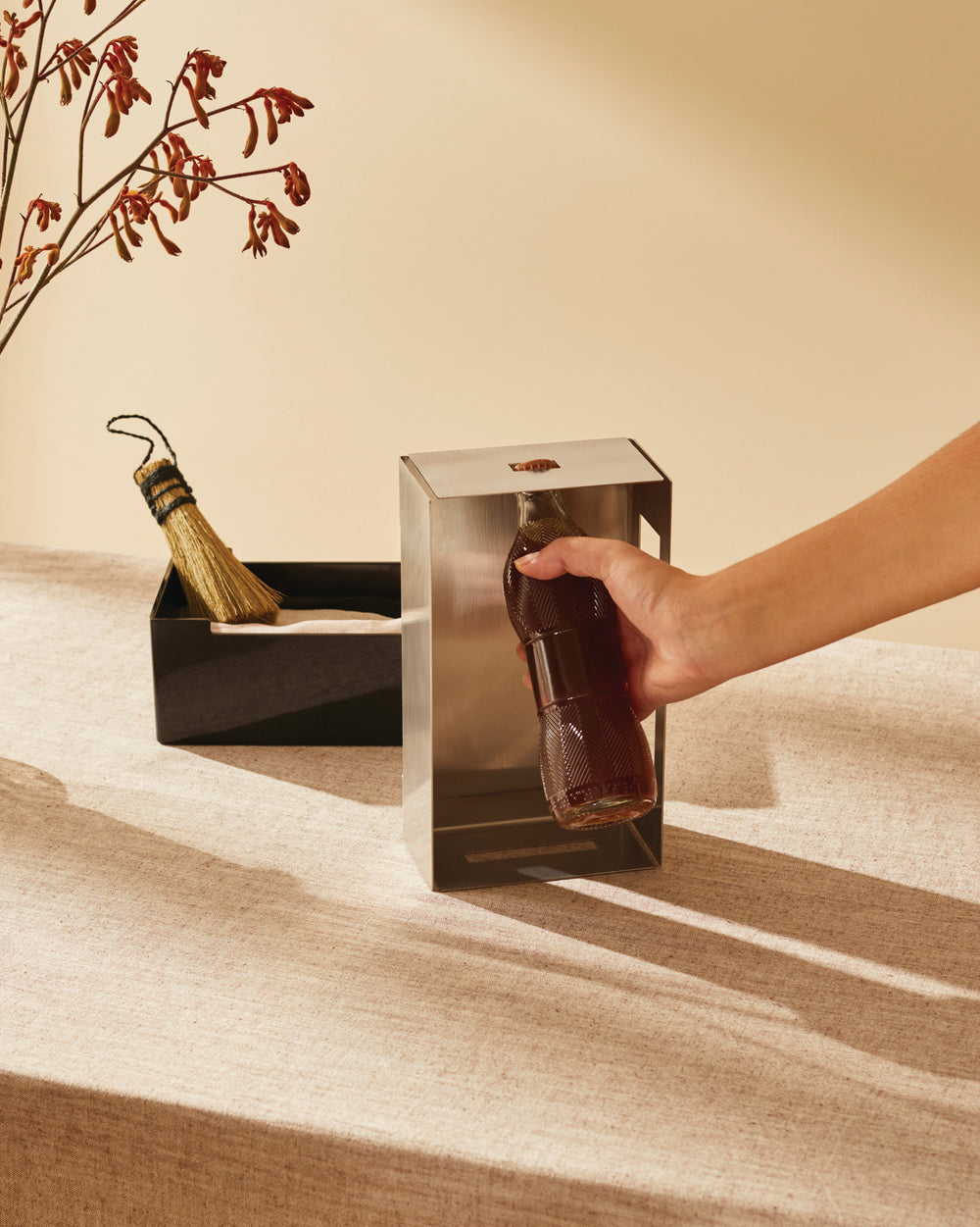 Stainless steel bottle opener and cap collector by Alessi, with a hand placing a dark bottle into its opening.
