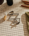 Metallic Socrates corkscrew by Alessi with a folding geometric design on a plaid tablecloth.