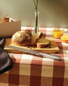 Silver-toned serrated bread knife by Alessi, lying on a wooden cutting board with a sliced loaf of bread.