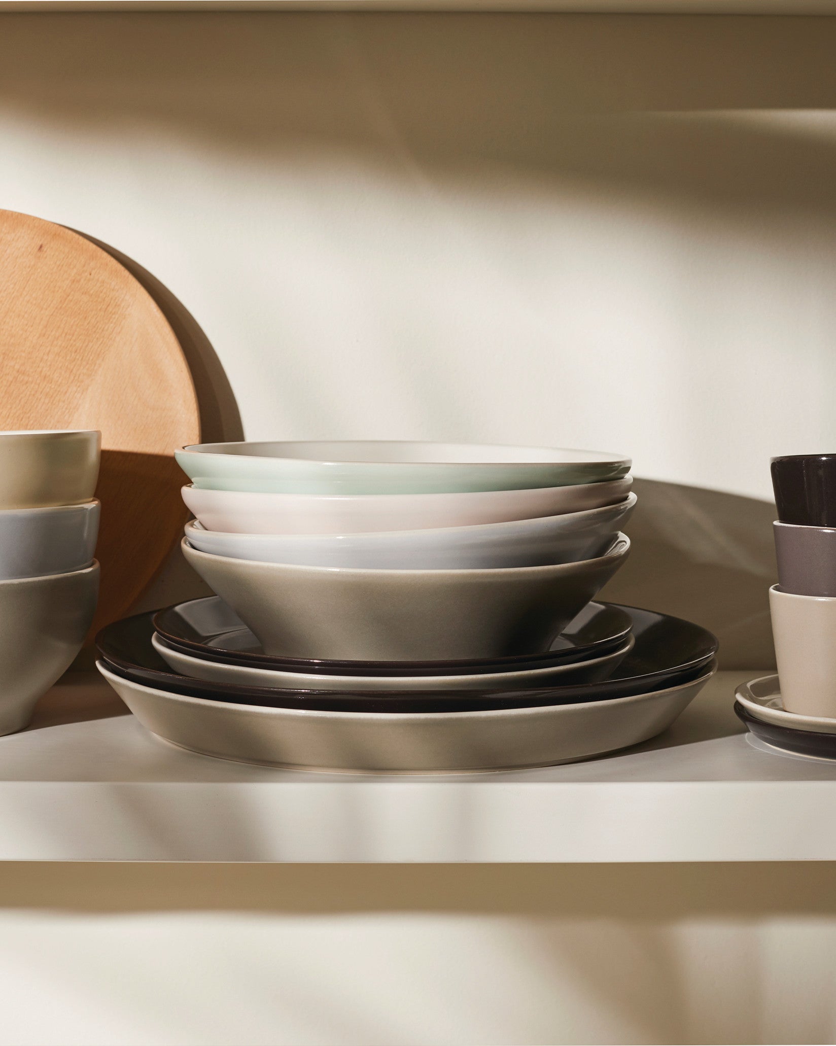 Assorted ceramic bowls and plates by Alessi in various neutral and pastel tones, neatly stacked on a shelf.