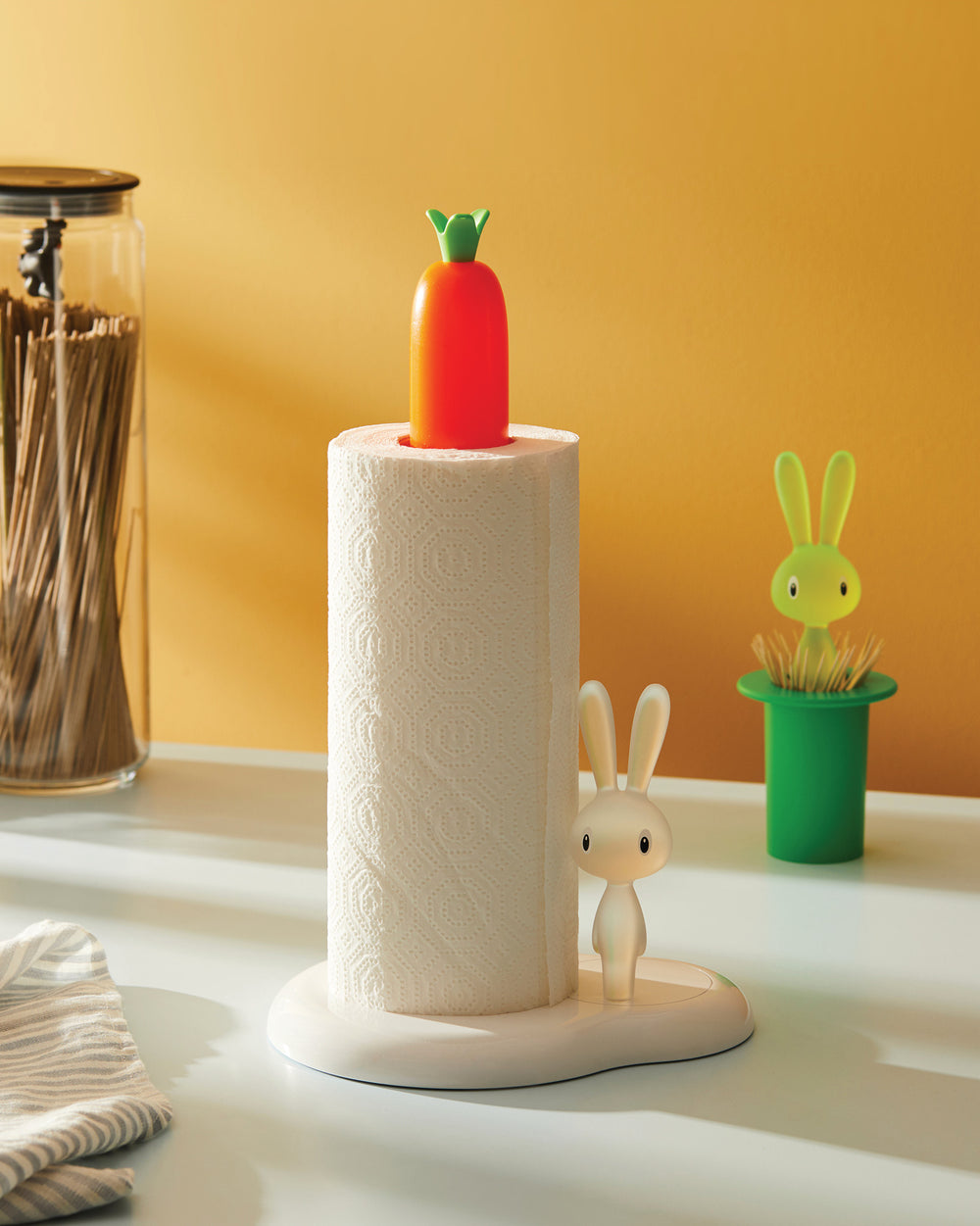 White Bunny & Carrot paper towel holder by Alessi, with an orange carrot finial and a white bunny figurine, on a countertop.