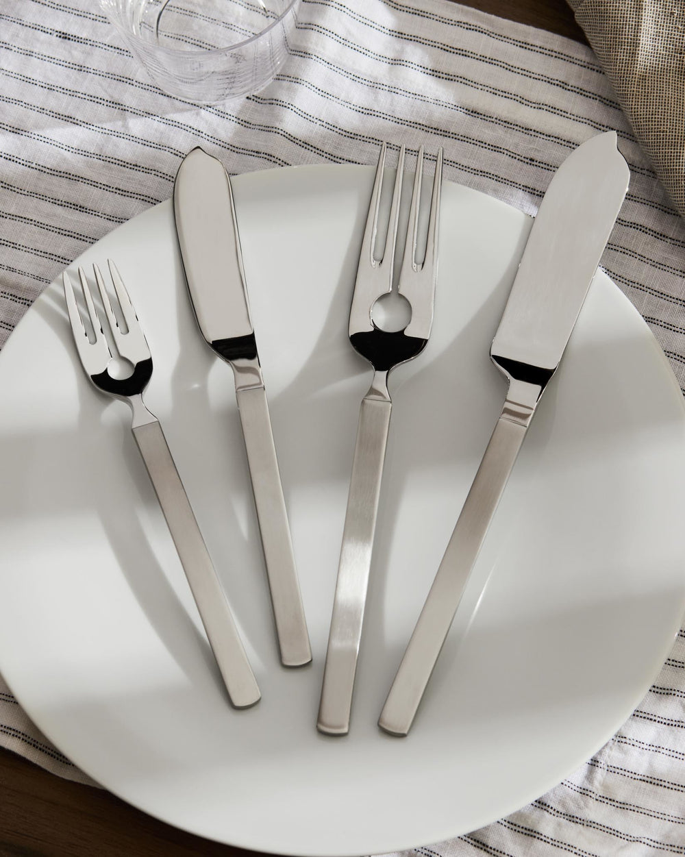 Silver fish cutlery set by Alessi on a white plate with a striped napkin.